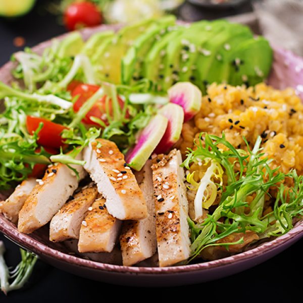 Healthy salad with chicken, tomatoes,  avocado, lettuce, watermelon radish and lentil on dark background.